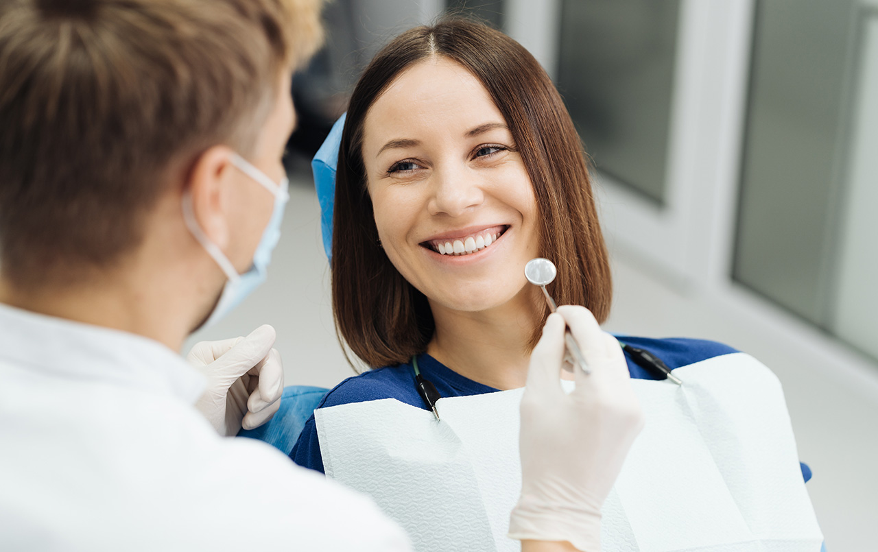 A woman at the dentist's office smiles brightly while a dentist, wearing gloves and a mask
