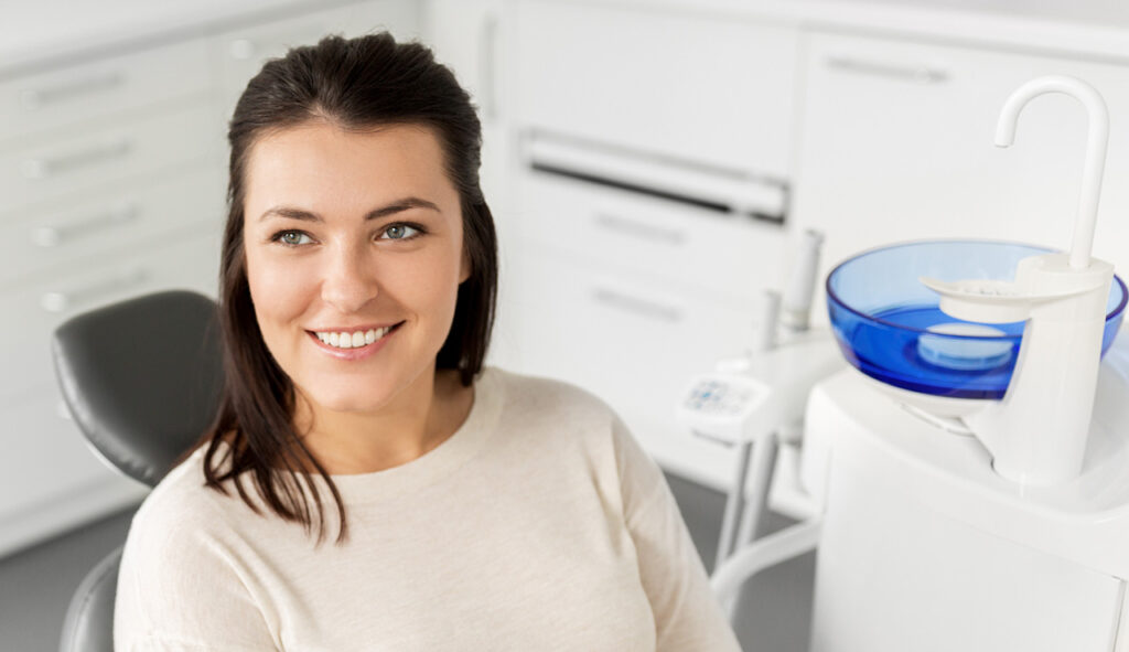 Smiling woman sitting in a dental chair, wearing a light sweater.