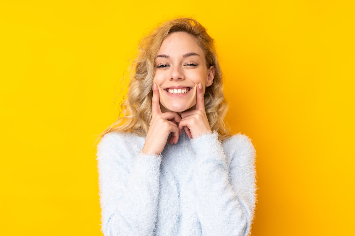 Young blonde woman isolated on yellow background smiling with a happy and pleasant expression